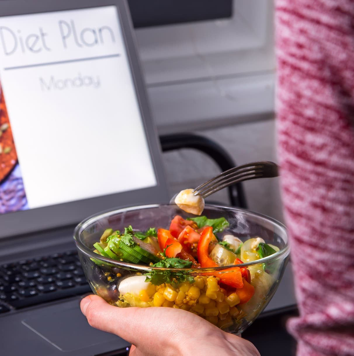 Laptop showing a weekly diet plan beside a salad bowl