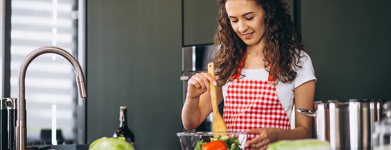 Woman in an apron preparing a salad in her kitchen
